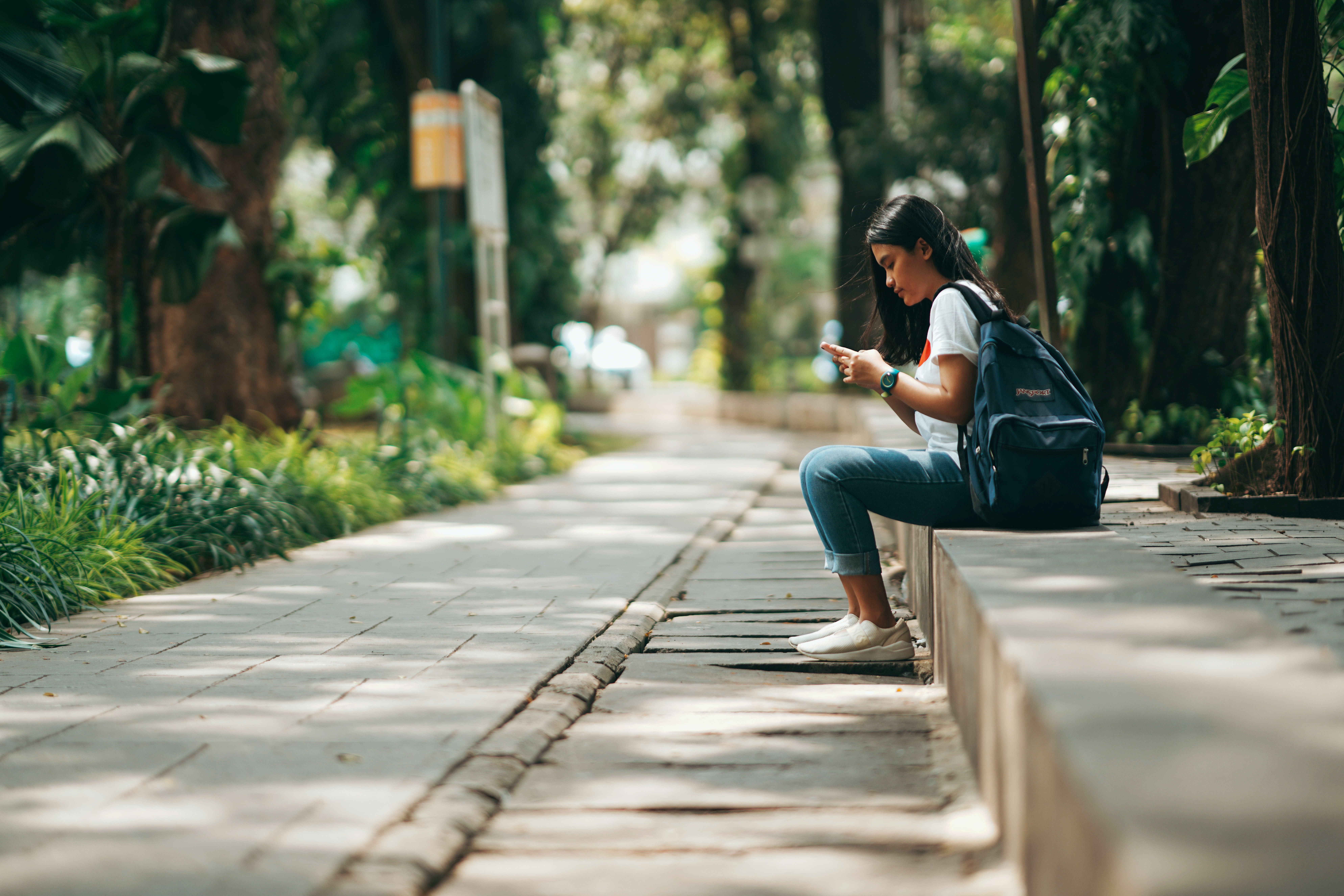 A girl texting while sitting on the pavement