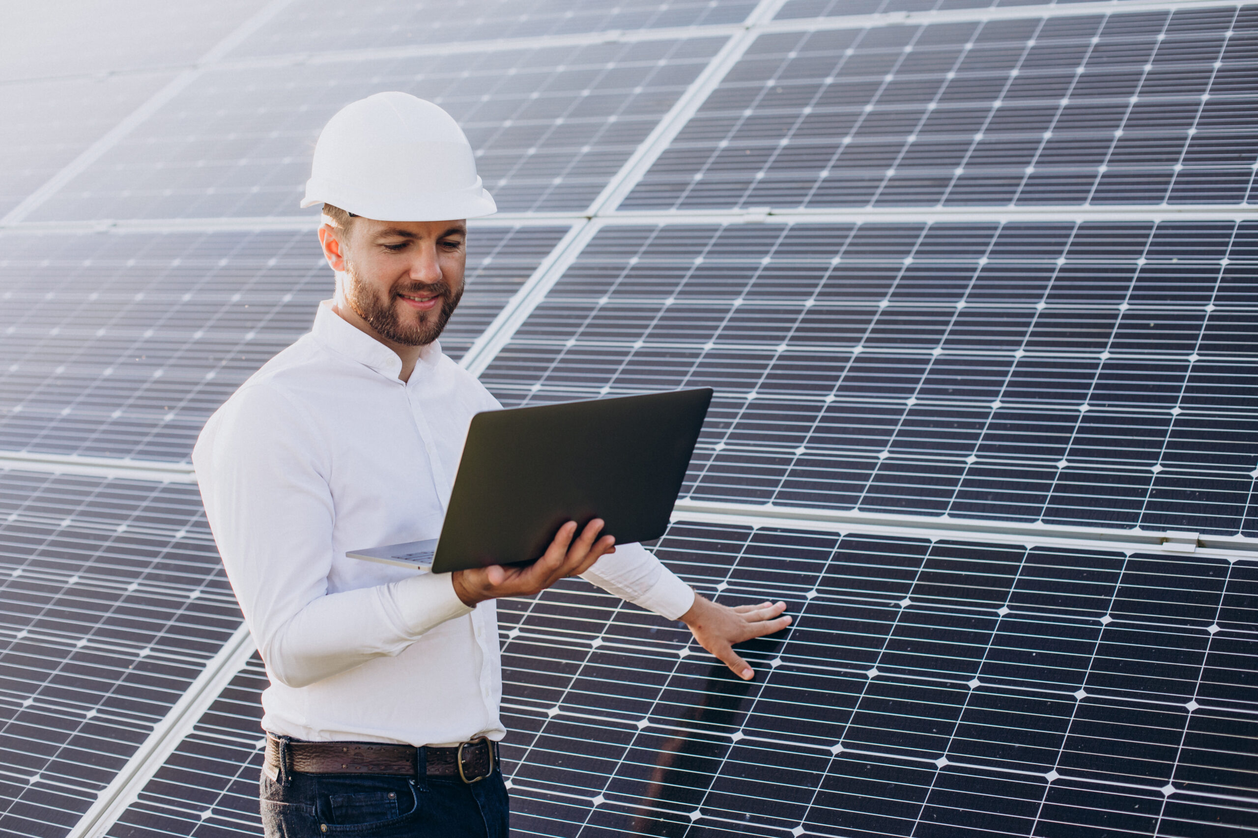 Young architect standing by solar panels making diagnostics on computer