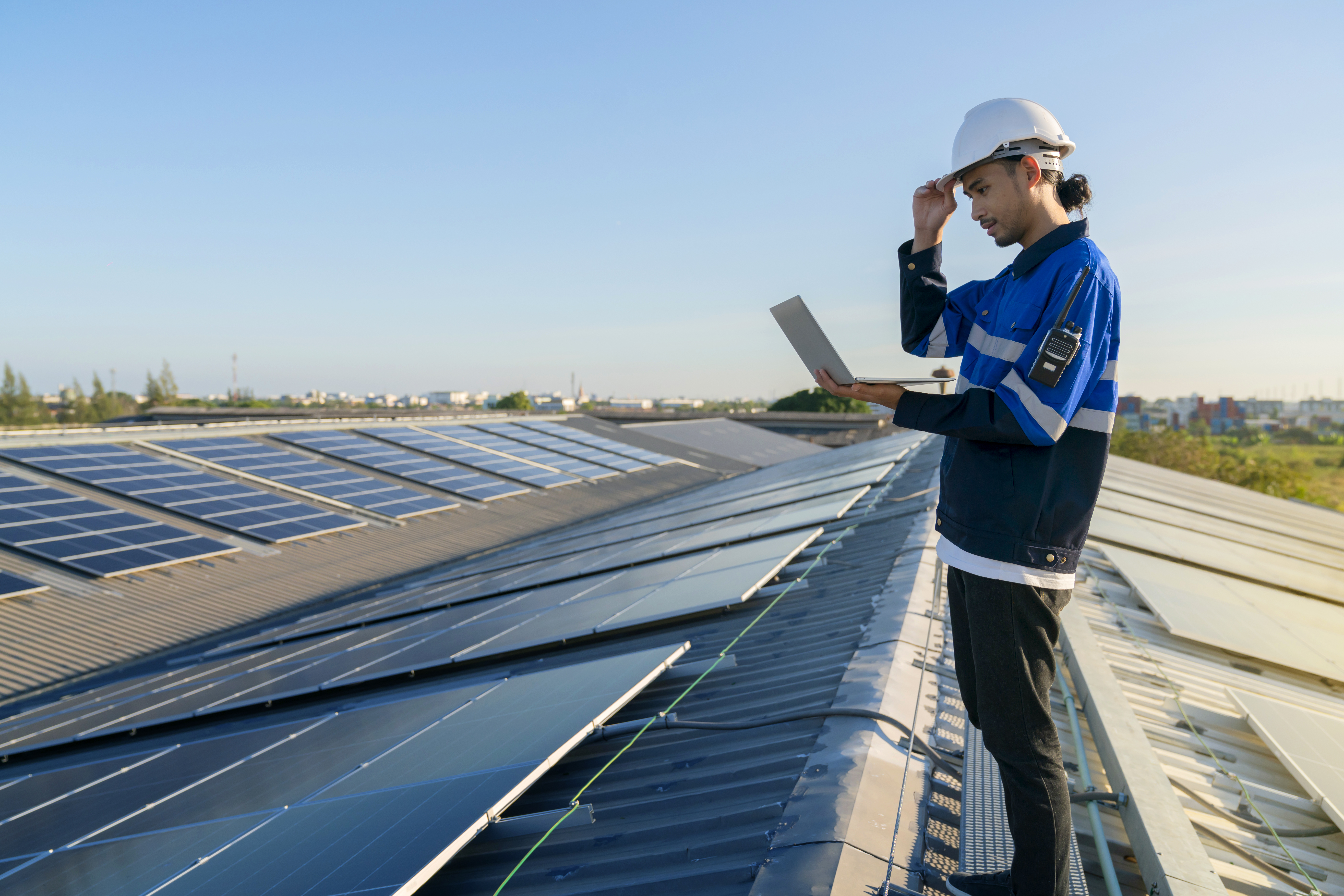 Specialist technician professional engineer with laptop and tablet maintenance checking installing solar roof panel on the factory rooftop under sunlight. Engineers holding tablet check solar roof.